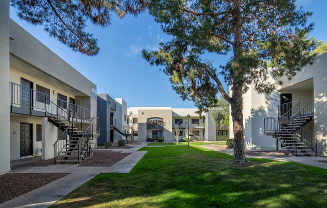 A tree stands in front of a white building with a metal staircase.
