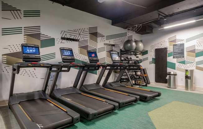 a row of treadmills in a gym with a wall mural of gym equipment