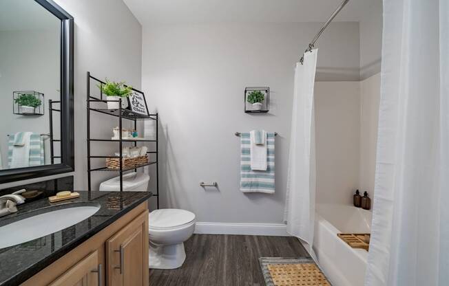 Bathroom vanity with framed mirror hung above. Toilet to the right. Tub/Shower can be seen in mirror reflection.