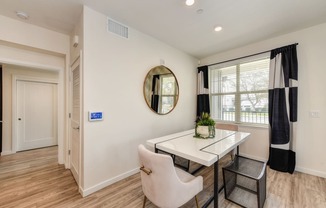 Dining area with table, chairs and potted plant on the table. Large window with curtains overlooking the entrance at Morgan Ranch Apartments, Morgan Hill