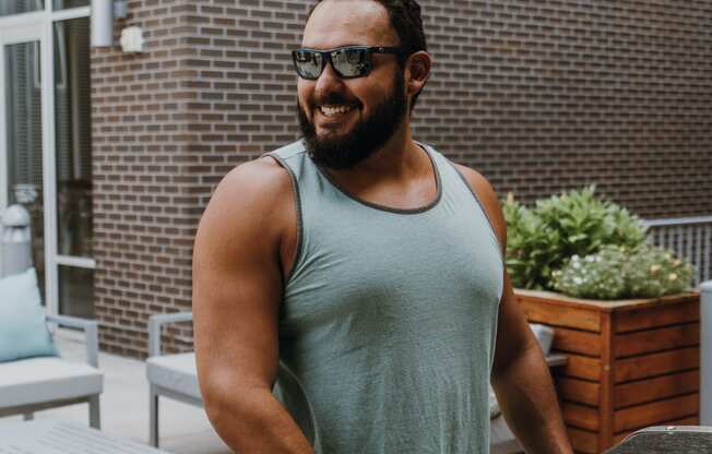 a man wearing a tank top and sunglasses standing next to a car