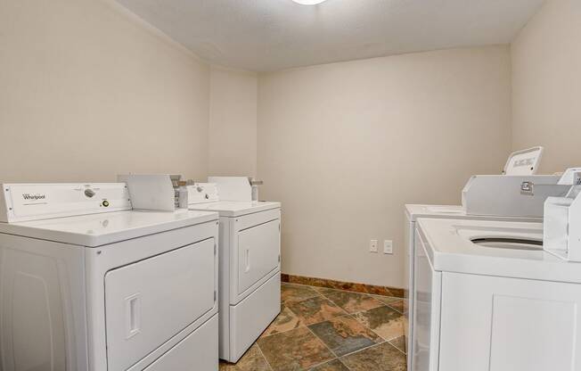an empty laundry room with four white washers and dryers and two sets of