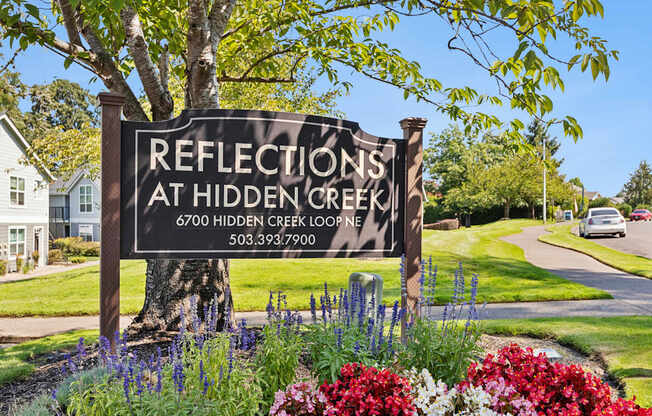 A sign for Reflections at Hidden Creek is surrounded by flowers and greenery.