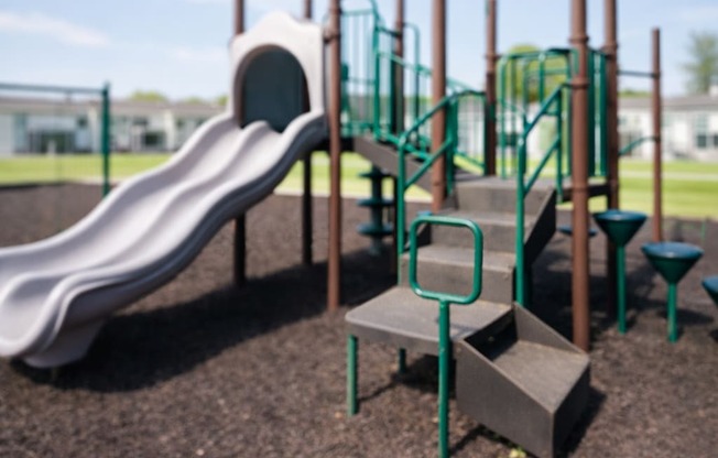 A playground with a slide, stairs, and a green railing.