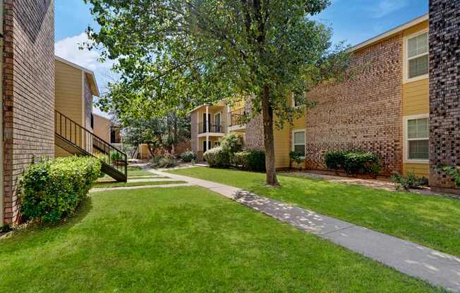 A well-maintained courtyard here at The Bradford with green lawns, mature trees, and paved walkways connecting the apartment buildings. A calm, open layout with surrounding residences and balconies creates a pleasant and welcoming outdoor environment.