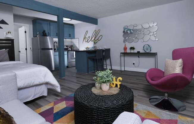 Fusion Las Vegas studio apartment with colorful geometric rug, fuchsia living room chair, and potted greenery on wicker coffee table.