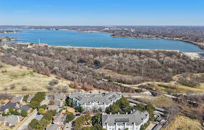 A large house with a grey roof is surrounded by trees and a body of water.