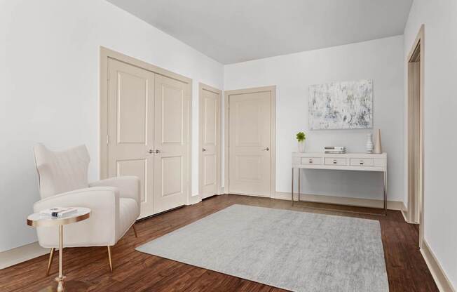 A white chair sits in a room with a grey rug and a painting on the wall.