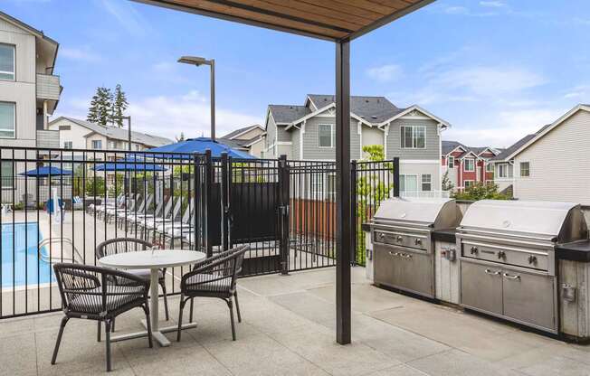 A patio with a table and chairs is surrounded by a pool and houses.