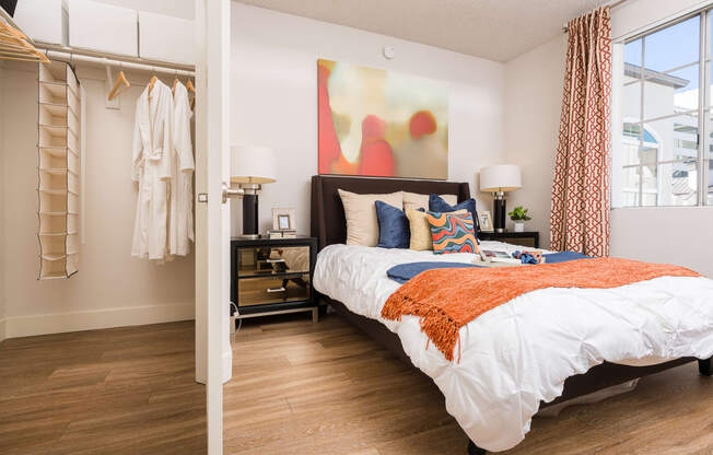 Studio Apartments in Miracle Mile Los Angeles, CA - The Preston - Bedroom with Plank Wood Style Flooring, Bed, Large Closet, Nightstands with Lamps, Framed Art, and Window with Curtains