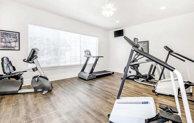 Fitness center with cardio machines and large window with wall mounted television and ceiling fan with light