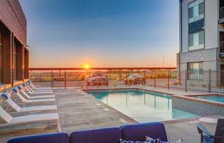 A sunset view from a rooftop pool area with lounge chairs and a fence.