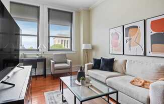 A living room with a grey couch, a glass coffee table, and a painting on the wall.