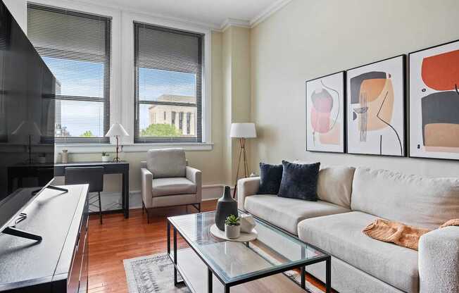 A living room with a grey couch, a glass coffee table, and a painting on the wall.