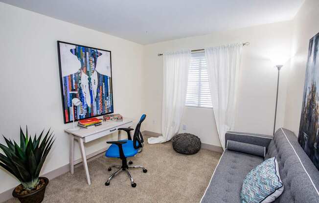 A room with a desk, chair, and a painting of a shirt on the wall.