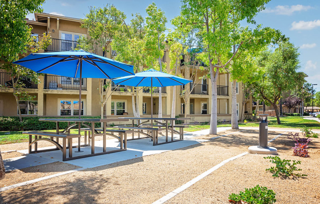 a picnic area with benches tables and umbrellas in front of an apartment building