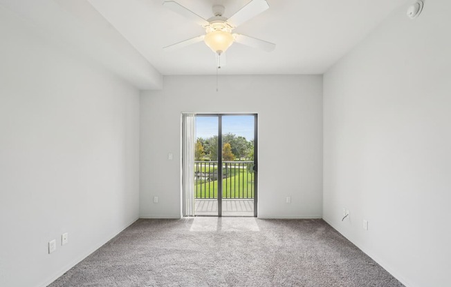 A room with a ceiling fan and a sliding glass door leading to a backyard.