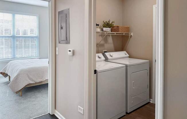 A small bedroom with a bed, laundry basket, and washing machine.