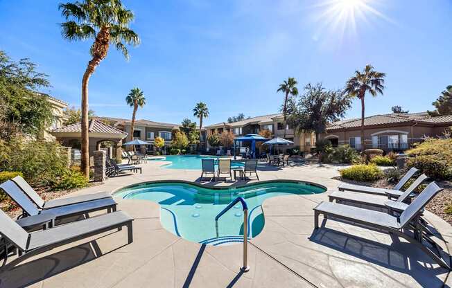 A sunny day at the pool with lounge chairs and palm trees.
