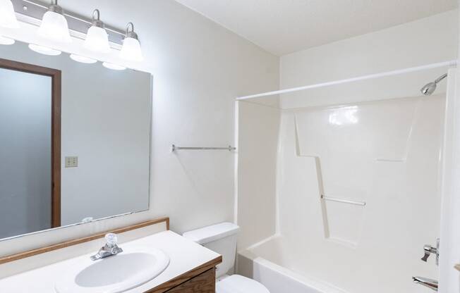 a bathroom with a shower sink and mirror and a toilet. Fargo, ND Rosegate Apartments