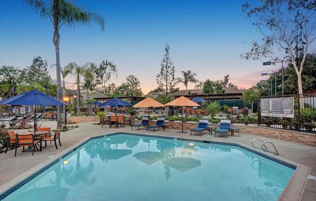 A large swimming pool surrounded by blue umbrellas and wooden benches.