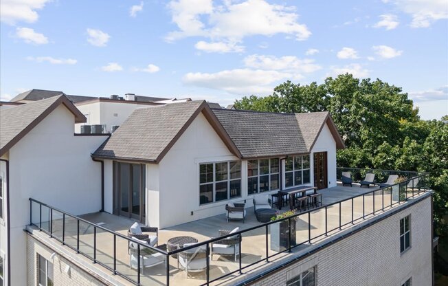 A white house with a black roof and a balcony with chairs and a table.