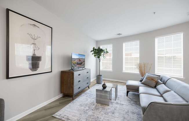 A living room with a grey sofa, a grey rug, a wooden cabinet, a side table, a potted plant, and a framed picture on the wall at Harbor Pointe Apartments, New Jersey