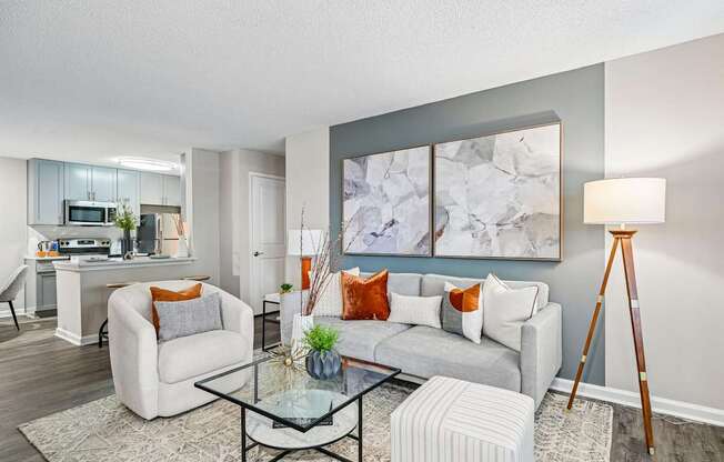 A living room with a grey sofa, a glass coffee table, and a large abstract painting on the wall.