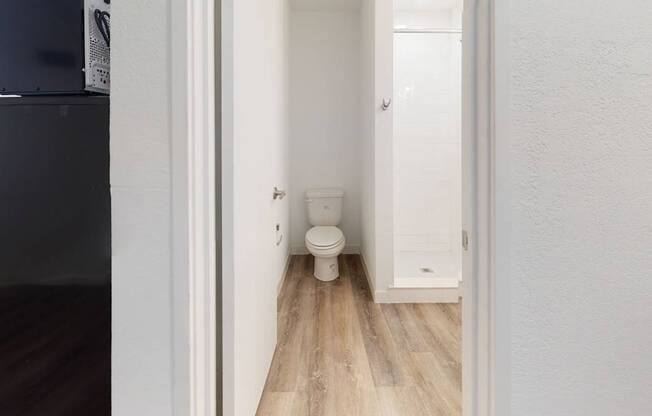 A white toilet in a narrow hallway with wood flooring.