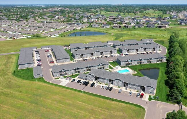 an aerial view of a group of houses near a field and a pond