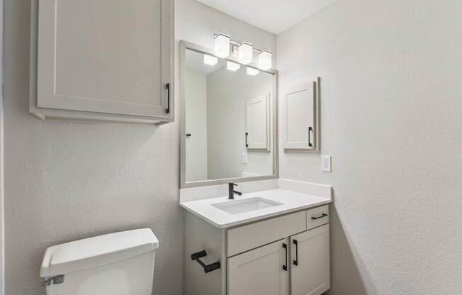 A white bathroom with a toilet, sink, and mirror.