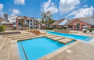 A large outdoor swimming pool with loungers and a building in the background.