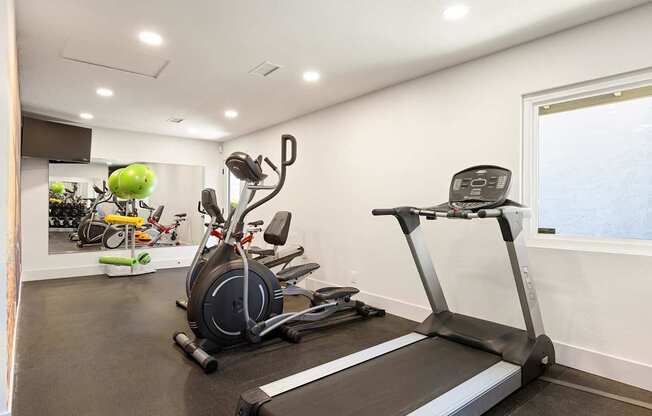 A home gym with a treadmill, exercise bike, and other equipment.