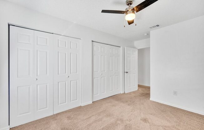 an empty bedroom with a ceiling fan and white closets