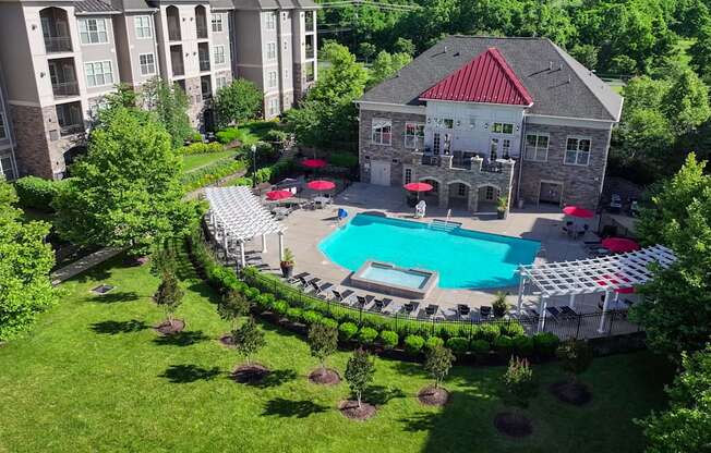 A large building with a red roof is surrounded by a pool and trees.