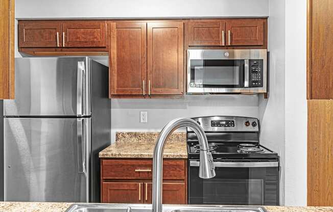 A kitchen with a refrigerator, microwave, oven, and sink.