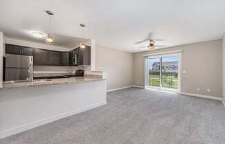 A spacious living room with a kitchen area and sliding glass doors leading to a balcony.