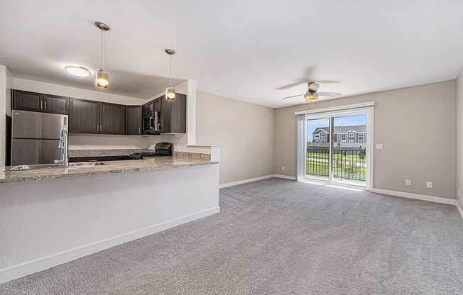 A spacious living room with a kitchen area and sliding glass doors leading to a balcony.