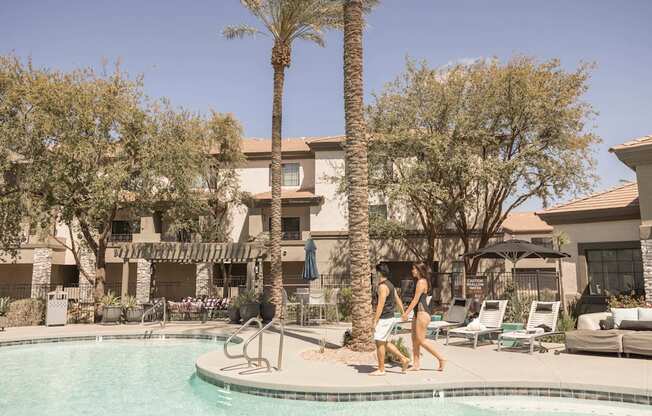 Two people walking by a pool on a sunny day.
