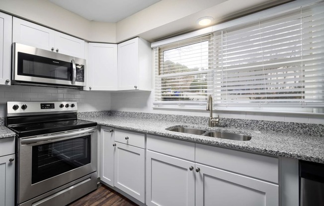 kitchen with white cabinets, granite counter tops, stainless steel appliances and large window above sink area