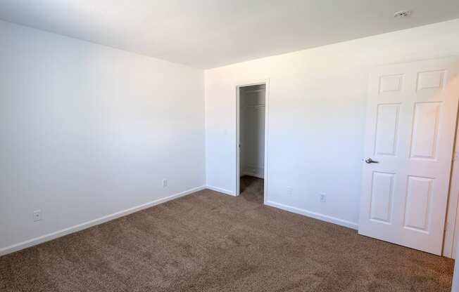 a bedroom with white walls and carpet and a door to a closet