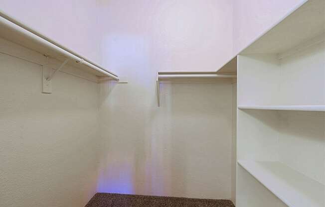 a walk in closet with white walls and shelves and two white shelves on the wall