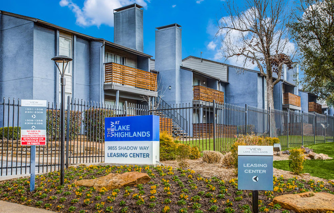 a blue and white sign is in the middle of a garden in front of an apartment building