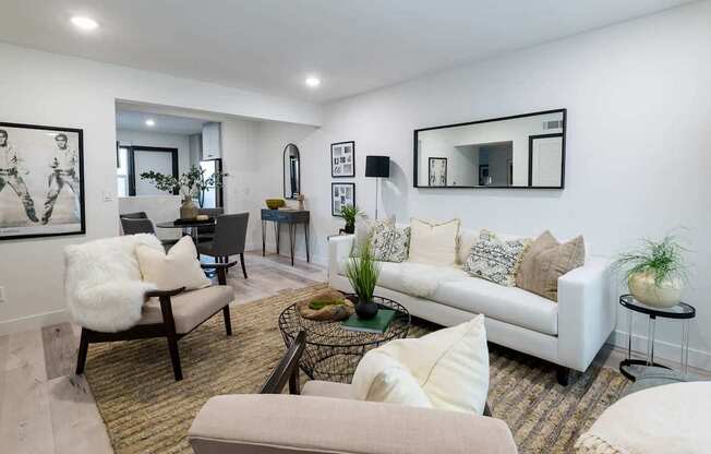 A living room with a white couch, a chair with a white fur throw, and a coffee table with a plant on it.