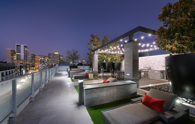 A landscaped rooftop entertaining area with a dining table, grilling station, and several lounge chairs facing a city skyline view.