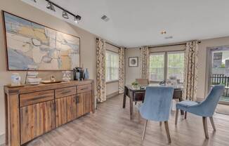 A room with a wooden cabinet, a table with two chairs, and a painting on the wall.
