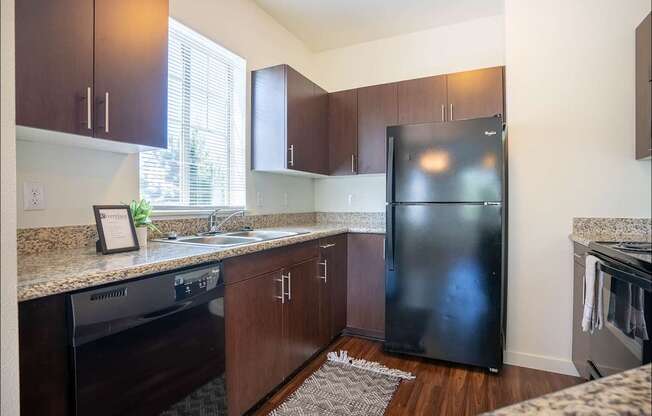 A kitchen with a black fridge and wooden cabinets at Riverplace Apartment Homes, Independence