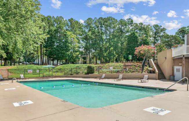 A large outdoor swimming pool surrounded by trees and a patio area with chairs and a table.