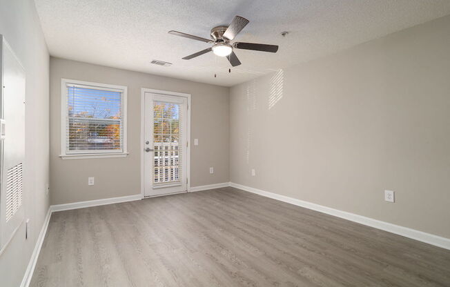 A room with a ceiling fan and light, hardwood floors, and a window with blinds.