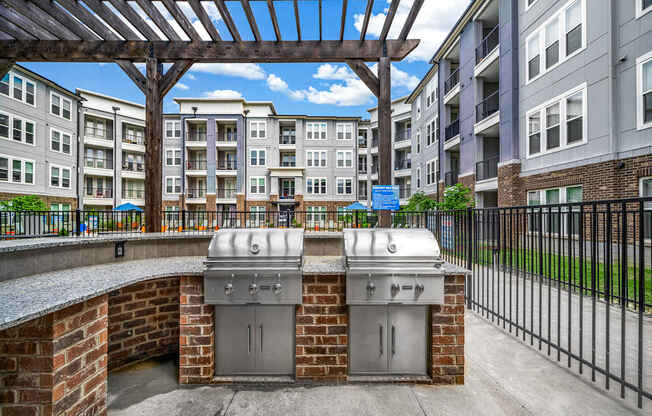 A patio with a grill and a brick wall with apartment buildings in the background.